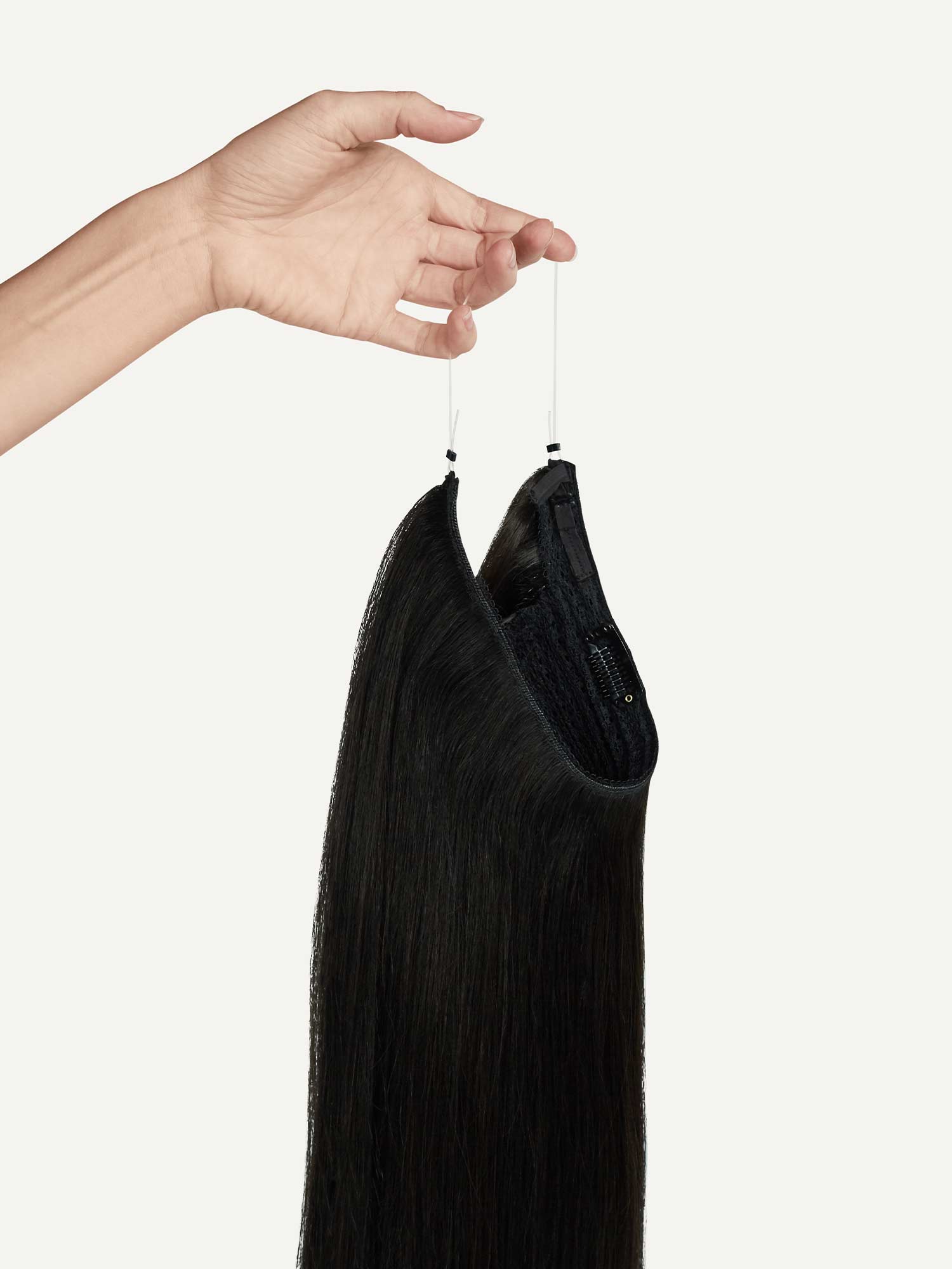 A hand holding a long black Luxy Hair Extension Halo.