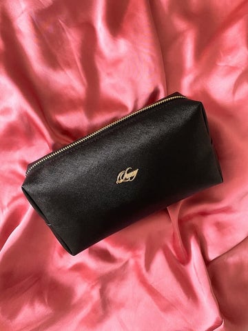 A black leather cosmetic bag on a pink satin cloth, perfect for storing beauty essentials.